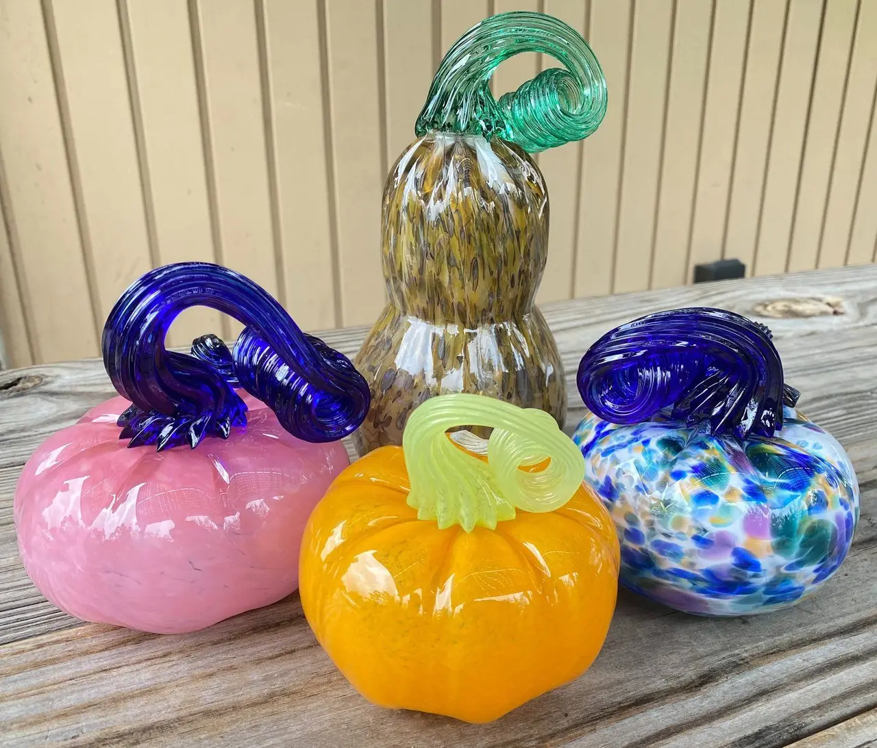 Student-made glass pumpkins and a gourd in pink, orange and swirled blue