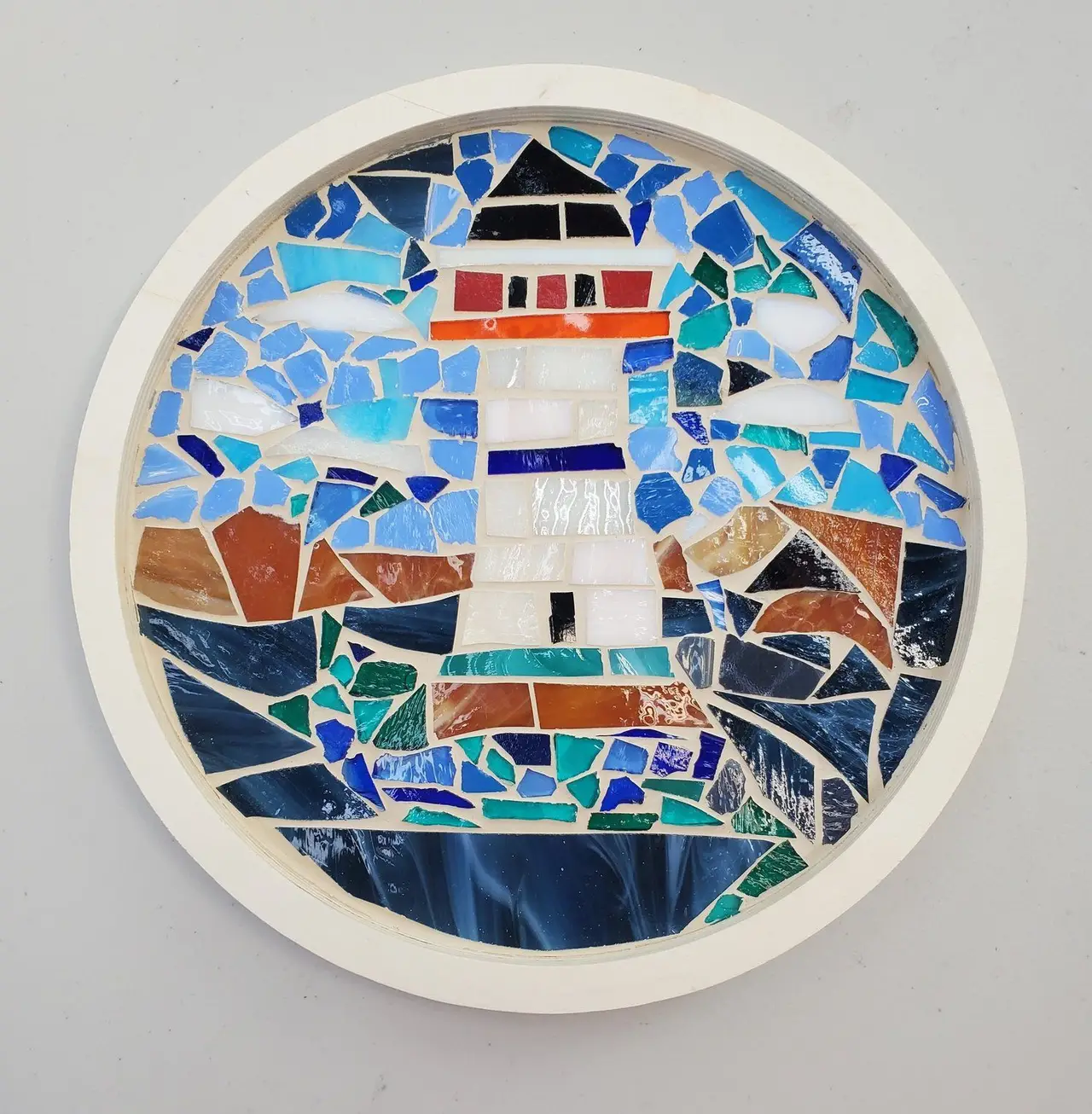 A round mosaic of a lighthouse on a rocky shore
