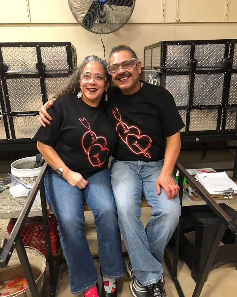 A smiling couple in matching heart T-shirts sit together in the studio
