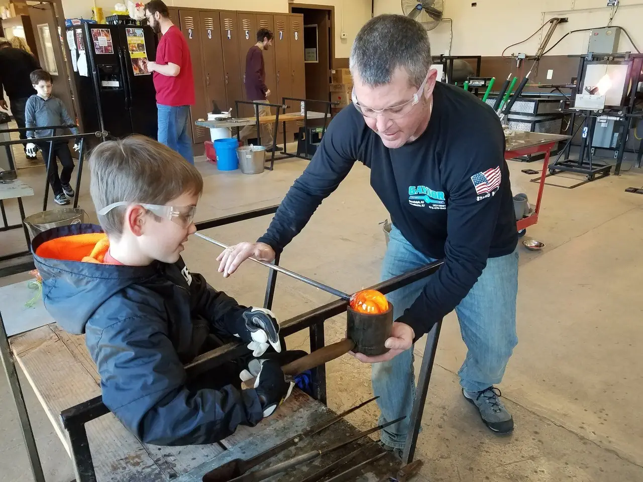 An instructor guides a young boy shaping a glowing galaxy globe at the bench